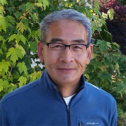 Portrait of scientist wearing glasses and blue sweater with trees in background