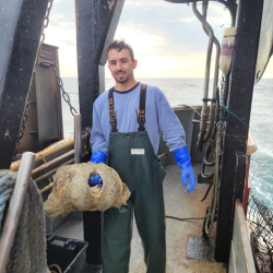 Vincent wearing blue gloves and waders on deck.