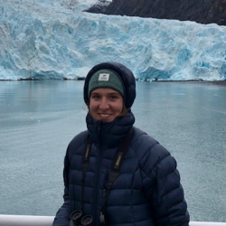 Kelley McBride in winter coat on deck with glacier in background.
