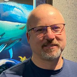 Man with glasses and blue shirt with whale poster in background 