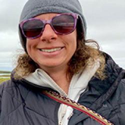 Woman with gray hat and glasses with landscape in background