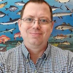Ken Brainard smiling in front of a fish poster