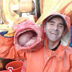 Man in orange coat with hood holding a large red fish 