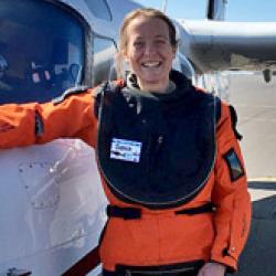 Woman with orange coat next to a plane 