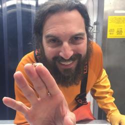 Brunette man with beard and orange suit holding up larvae 
