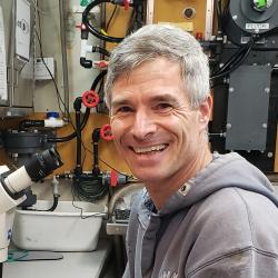 Scientist with gray jacket in front of microscope in a lab