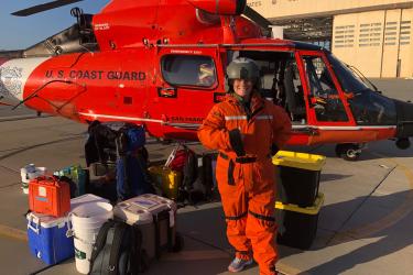 A woman scientist in flight gear in front of a U.S. Coast Guard helicopter.