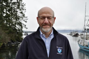 Jon Kurland posing for his headshot with trees, water, and boats in the background