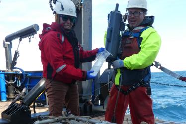 Two scientists extracting eDNA from Niskin bottle water sample.