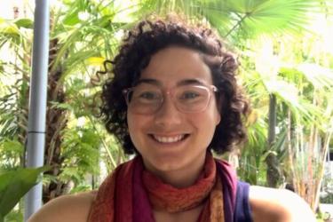 In this selfie, Adyan has light olive skin and chin-length curly dark-brown hair. She is wearing pink glasses and a fuschia, orange and purple scarf.