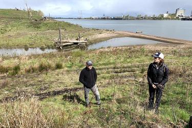 Two people stand on a grassy hill near a river