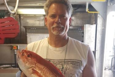 Kevin Rademacher posing with a large vermillion snapper inside the lab on a ship.