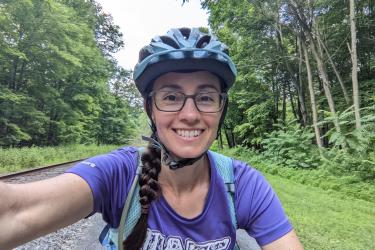 Selfie of woman wearing bike helmet riding her bike with trees and grass in the background