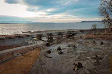 A railroad bridge runs parallel to the shore, with estuary habitat in the foreground and open water in the background