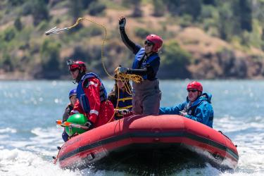 Kathi George aboard an inflatable boat tossing a hook into the water.