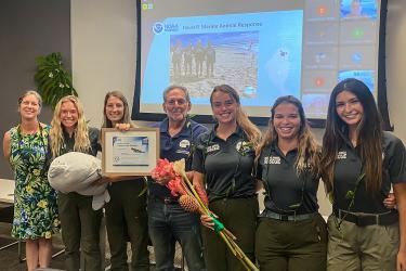 A group photo of seven taking a photo with a picture frame after receiving an award.