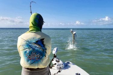 A fisherman catches a tarpon from his boat.