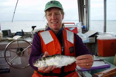 woman on a vessel wearing a life vest holding a silver colored fish