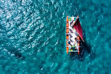A bird's-eye-view of eleven people on a canoe over clear blue waters.