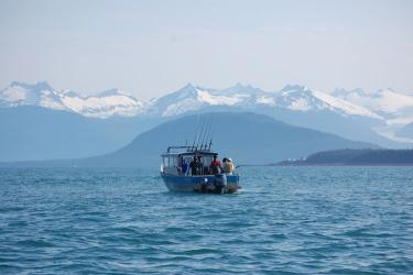 anglers on fishing boat surrounded by snow-capped mountains
