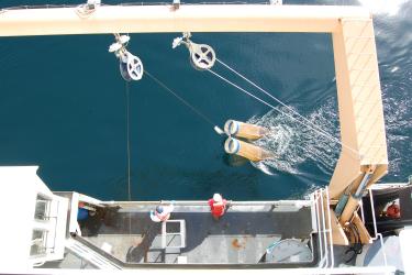 Looking down on two bongo nets being lowered over the side deck of a research ship. The nets are made of fine mesh and shaped like a funnel. The end of the funnel is closed. A round metal ring at the top keeps the net open.