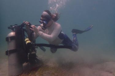 A woman underwater taking off scuba gear.