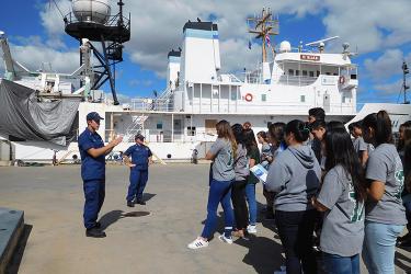 Two NOAA Corps officers speak to a group of high school students with the NOAA Ship Hi'ialakai in the background. 