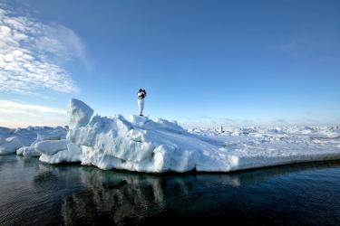 Scientist looking through binoculars on top of ice near water