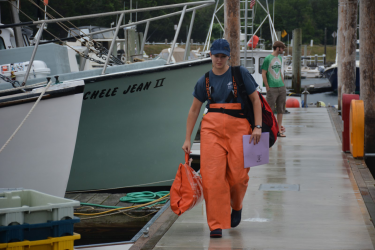 Observer in orange rain gear, with supplies walking on dock.