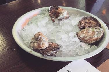 Raw oysters rest on a dish full of ice next to a Rappahannock Oyster Bar menu.