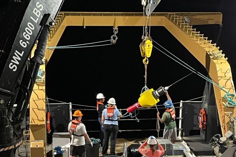 Researchers and technicians deploy an instrument off the back of a NOAA Ship