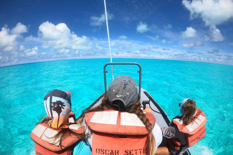 Three researchers drive a small boat on the open water, wearing PFDs that say "Oscar Sette."