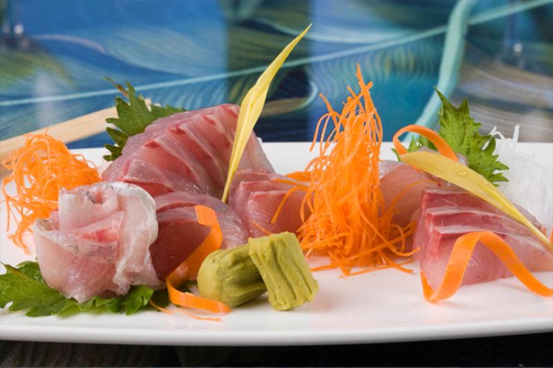 Thinly sliced cut fish on a plate garnished with vegetables and wasabi.
