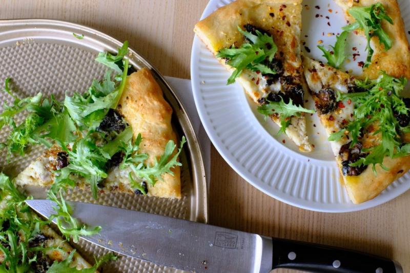 Slices of garlic chili oil and smoked oyster pizza on baking pan and a white plate, topped with fresh greens.