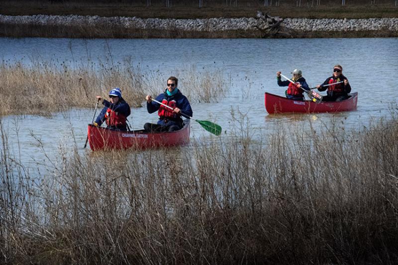 Four people in two red canoes paddle through a wetland