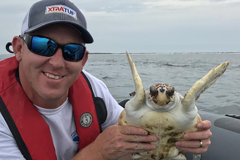 Jason Letort holds a juvenile loggerhead sea turtle during permitted work testing a turtle excluder device off the coast of Panama City, Florida.