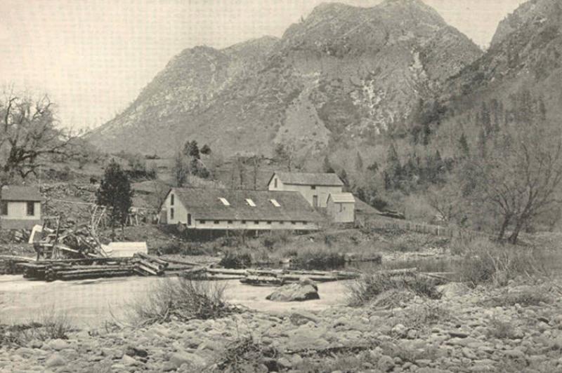 Wooden buildings of Baird Station, with McCloud River in the foreground, mountains behind