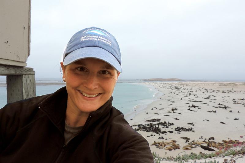 Woman wearing a cap looking a the camera with the shoreline visible in the background