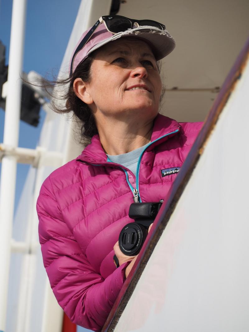 Photograph of Shannon Rankin at sea - she is holding a camera, getting ready to photograph marine mammals.