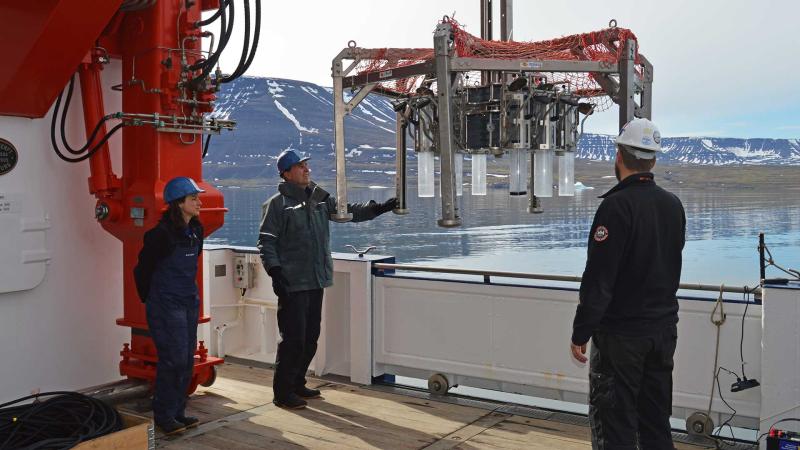 Threee people on a deck of a ship are deploying equipment over the side into the ocean.