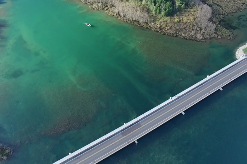 Aerial image of a river with a road spanning across it and a boat in the background
