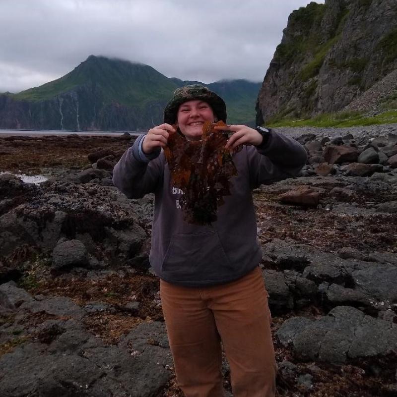 Woman holding up seaweed on an Alaska Beach.