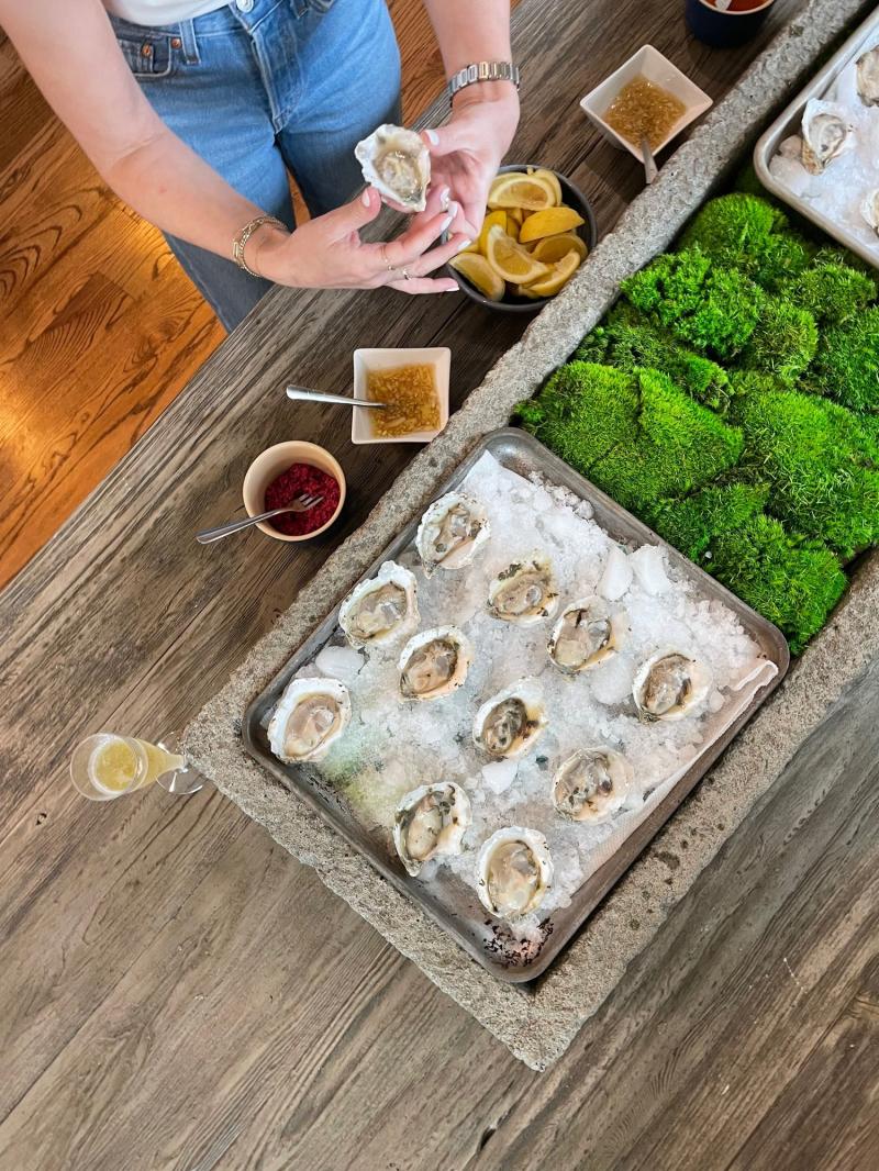 A raw bar with oysters on ice, next to a glass of champagne and two mignonette sauce options for the oysters.
