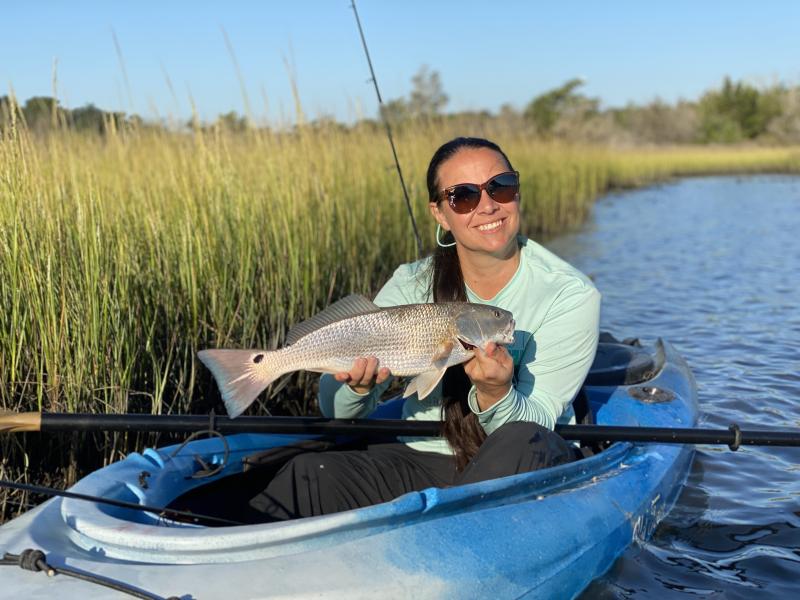 Woman holds a red drum while sitting in a blue kayak on the water