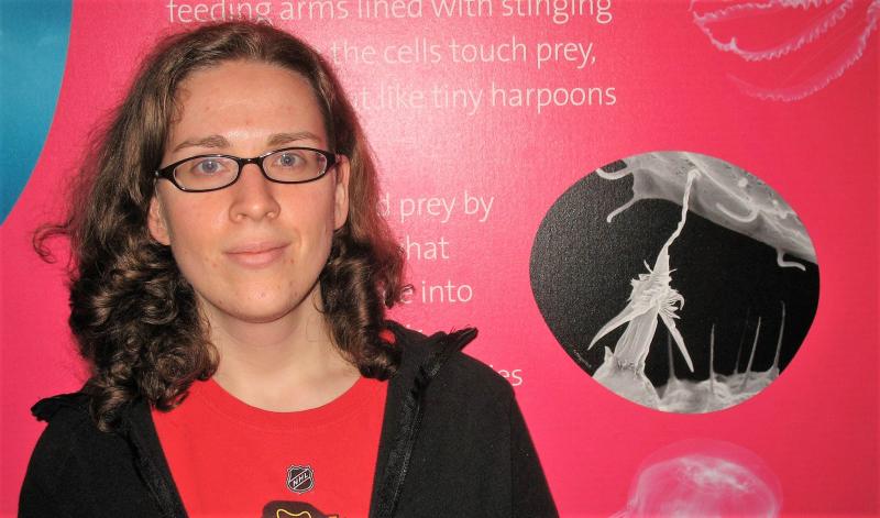 A woman poses in front of a poster featuring a black and white image of a nematocyst.