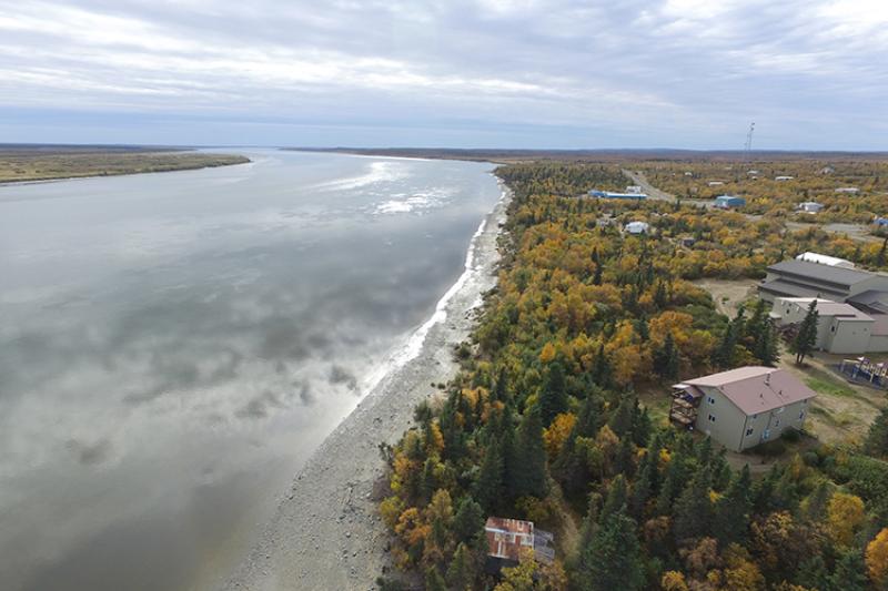 Aerial view of several buildings surrounded by forest on the shore of a wide river