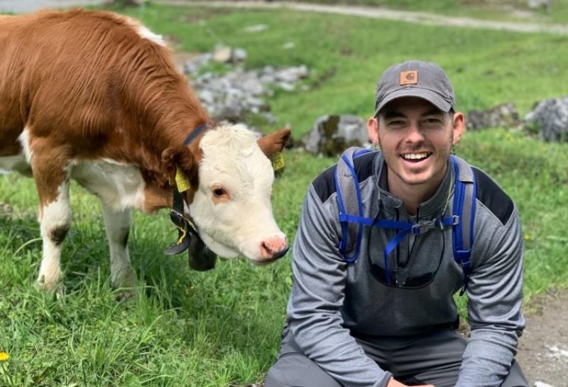 Michael Bradley crouching next to a cow that is brown and white 