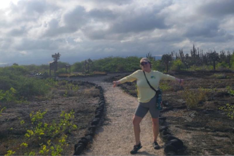 A woman stands smiling on a trail outside.