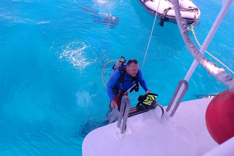 A man in scuba gear climbs out of bright blue water onto a boat.