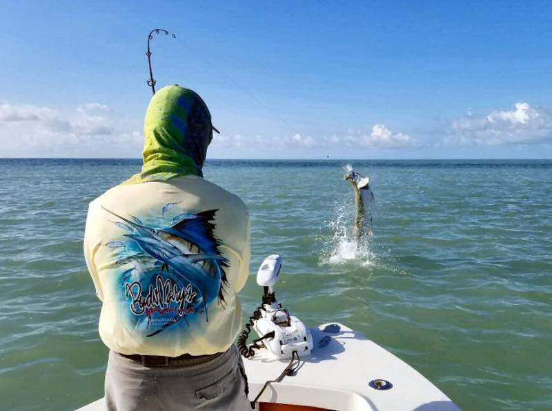 A fisherman catches a tarpon from his boat.